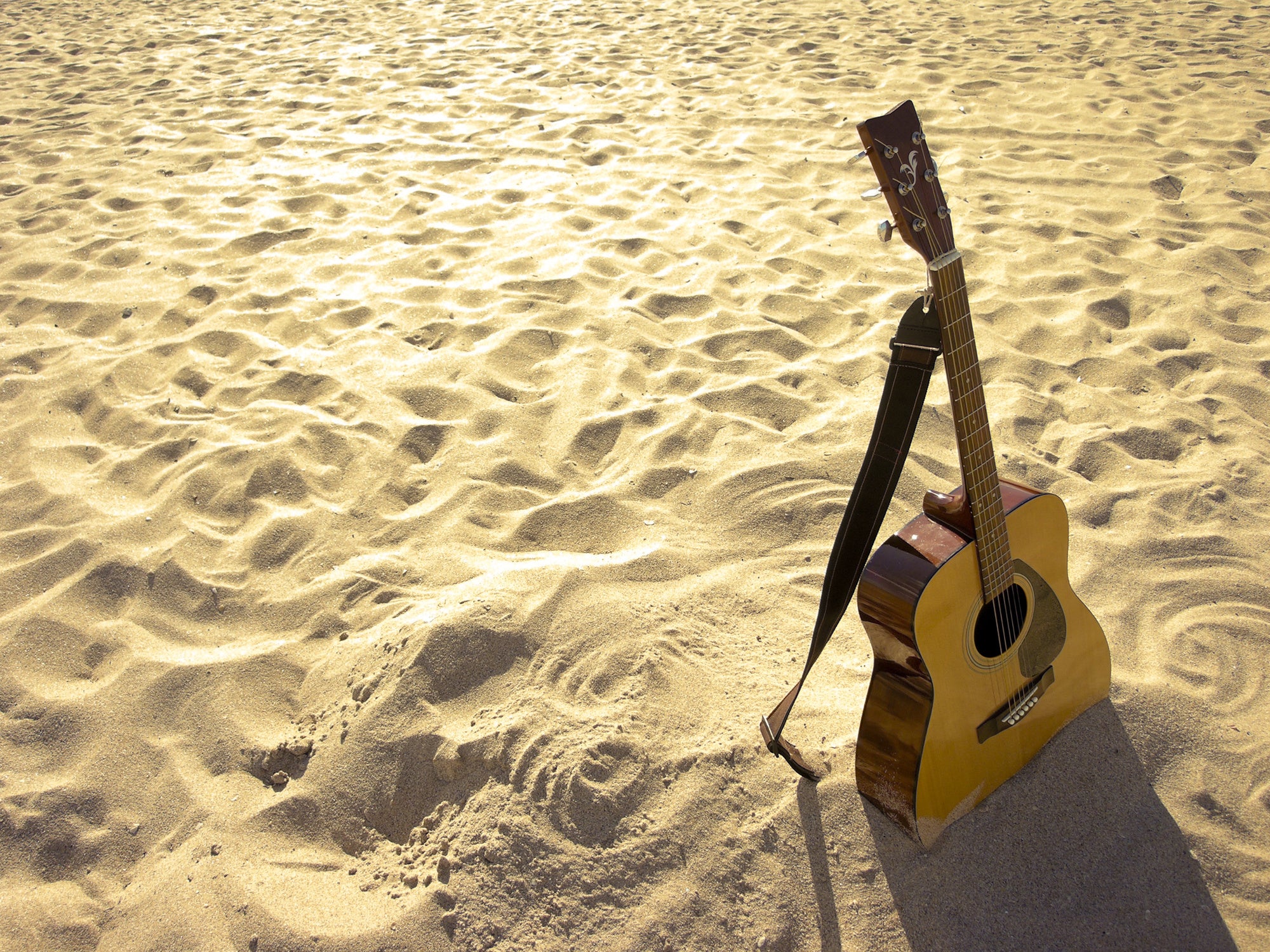 Guitar sitting in the sand with a guitar strap. 